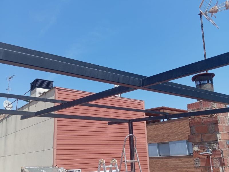 Estructura de vigas metálicas montada sobre una cubierta para formar una pérgola