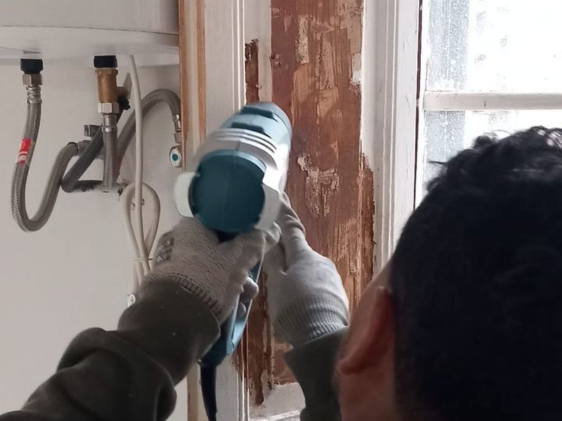Operario decapando con lijadora la pintura de una carpintería de madera para recuperarla