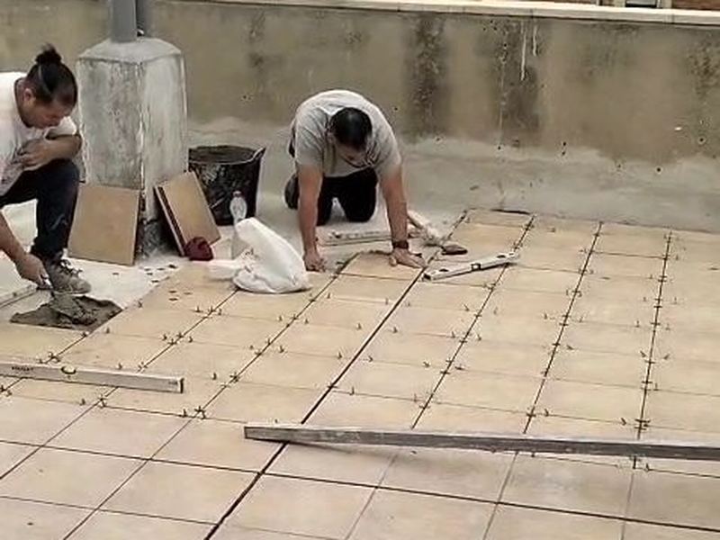 Dos operarios colocando el pavimento de gres de una terraza con crucetas y nivel